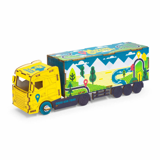 A wooden model of a large truck in bright yellow with a colourful patterned trailer featuring mountains and trees.