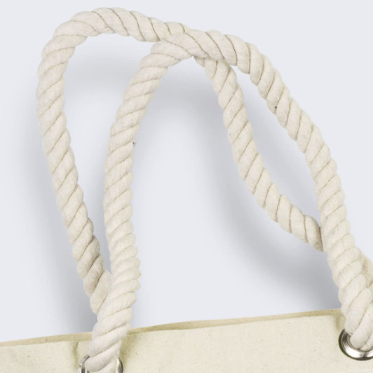 A close-up of the twisted, cream-coloured rope handles of a tote bag featuring silver eyelets.