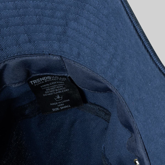A navy blue Yuma Bucket Hat with an inner label and a logo, made of 100% cotton.