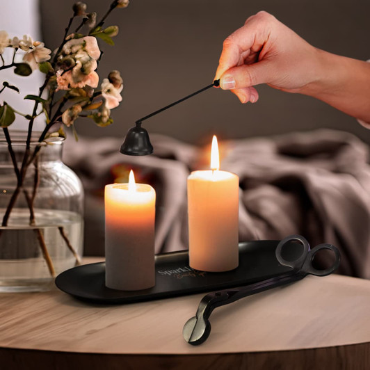 A candle accessory set in black featuring a candle snuffer and a wick trimmer, positioned next to lit candles on a tray.