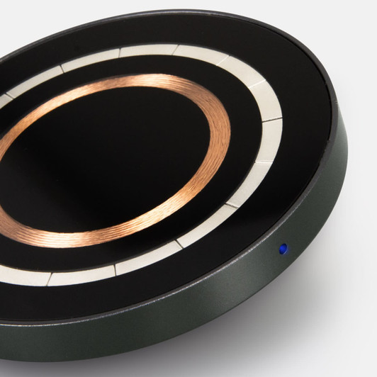 A wireless charger in black and green, featuring a copper circle design and a small blue indicator light.