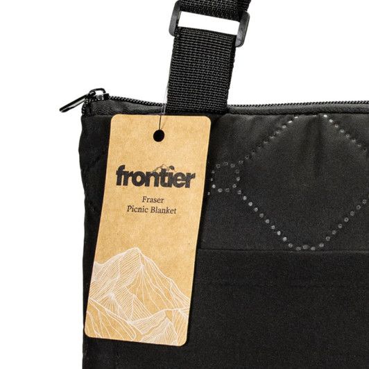 A black picnic blanket with a carrying strap and a tag featuring a brand logo.
