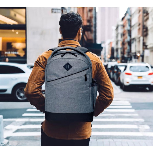 A grey backpack with black accents is worn by a person standing on a city street, facing away from the camera.