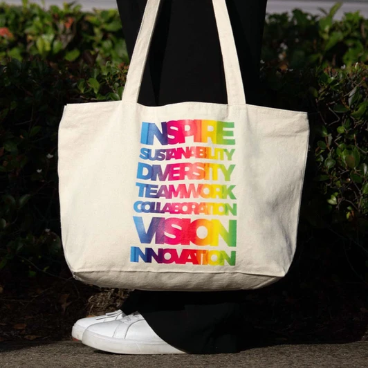 A zippered cotton canvas shopper tote in natural colour with a rainbow of text highlighting various positive themes.