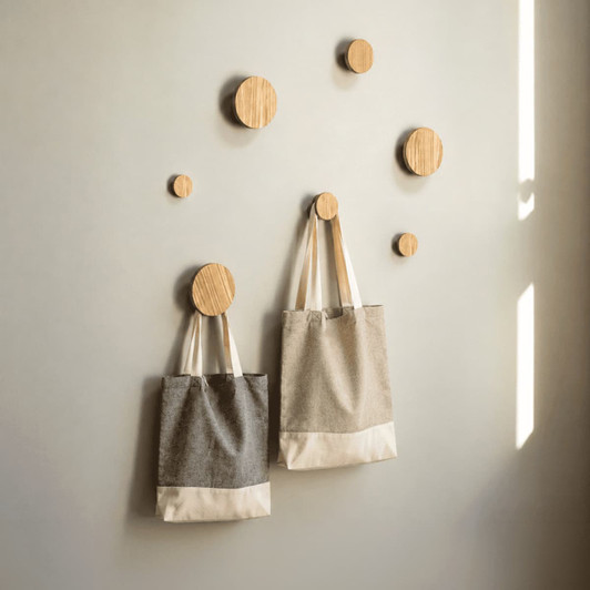 Two recycled cotton twill tote bags in grey and beige hanging on wooden pegs against a light wall.