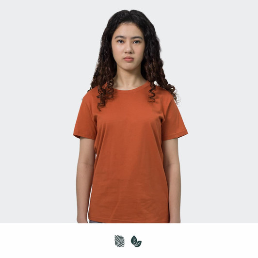 A woman stands wearing an orange TRENDSWEAR original women's T-shirt. The shirt has a simple design and a logo.