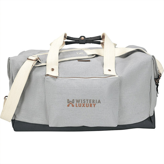 A grey cotton weekender duffel bag with cream handles and a branded pocket on the front.