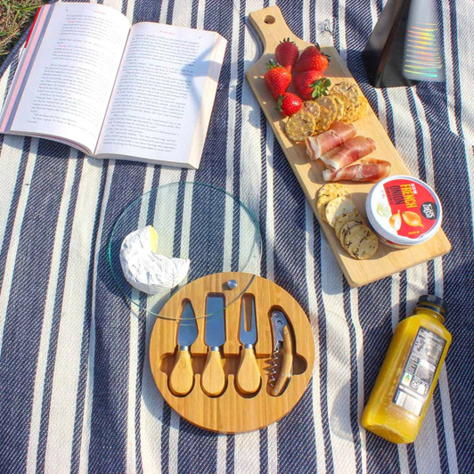 A wooden serving board with assorted snacks, including strawberries, crackers, and dips, on a striped blanket.