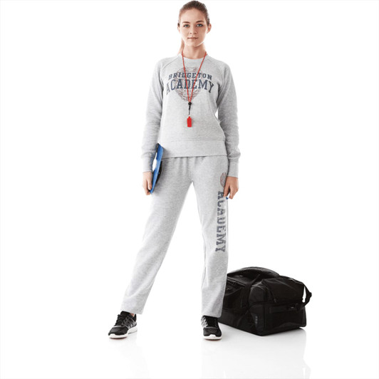 A woman in a grey fleece crew jumper and matching pants stands with a bag, holding a clipboard.