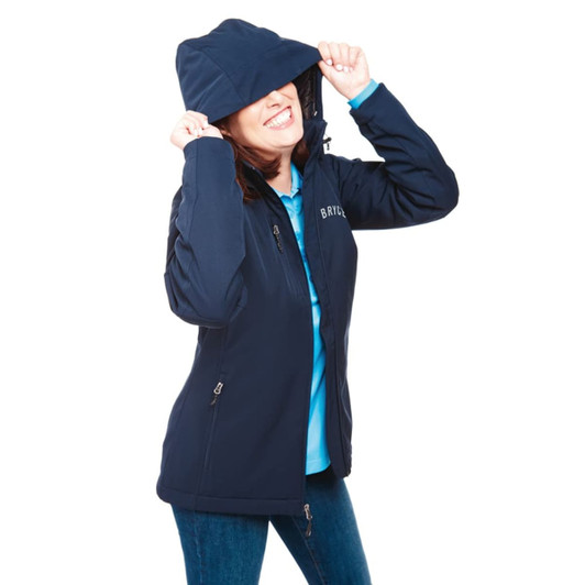 A woman wearing a navy softshell jacket with a hood, smiling and playfully pulling it over her face.