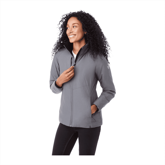A woman is wearing a grey insulated puffer jacket with a zippered front and pockets, featuring a logo.
