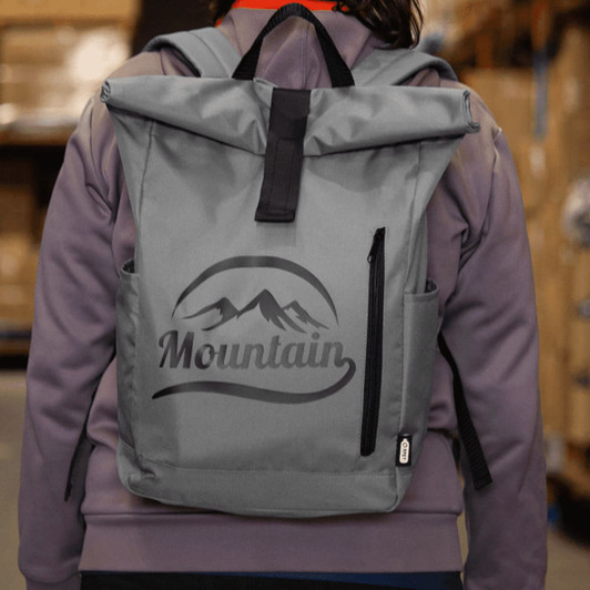A grey roll-top backpack with a logo, featuring two side pockets and adjustable straps.