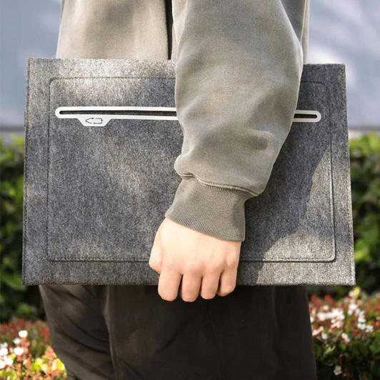 A grey felt laptop sleeve is held in one hand, featuring a sleek design and a logo.