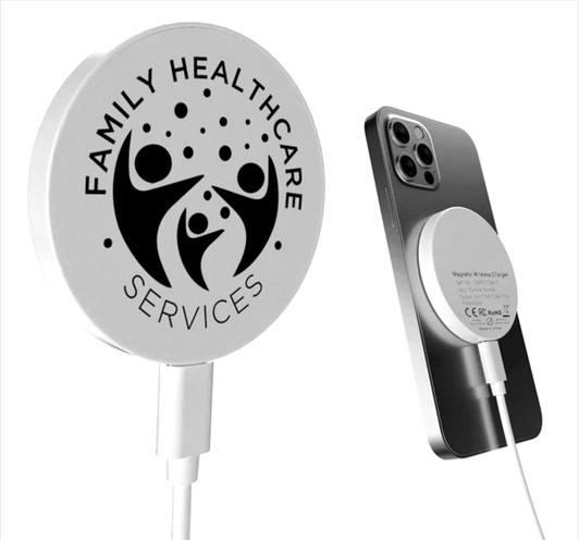 A white magnetic wireless charger with a logo, positioned next to a smartphone.
