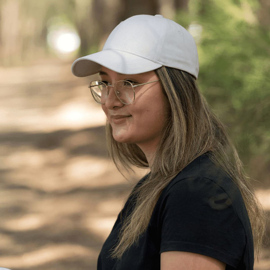 A woman with long hair wearing a white cotton twill cap, set in a natural outdoor background.
