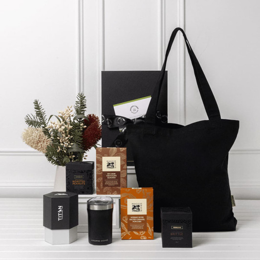 A black tote bag with assorted sweet treats, essential items, and a decorative floral arrangement.