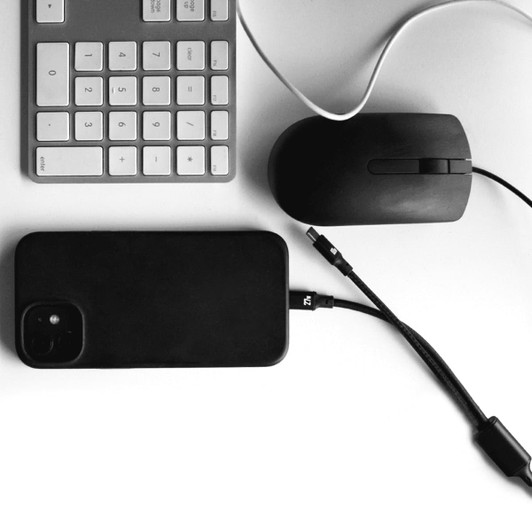 A black 4 in 1 fast charging data transfer cable next to a black phone, mouse, and keyboard on a white surface.