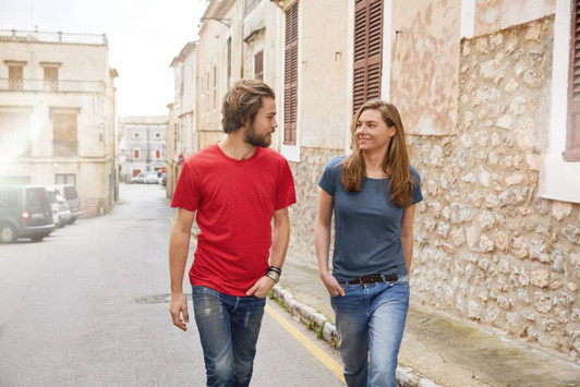 A red men's t-shirt and a blue women's t-shirt worn by two people walking together on a street.