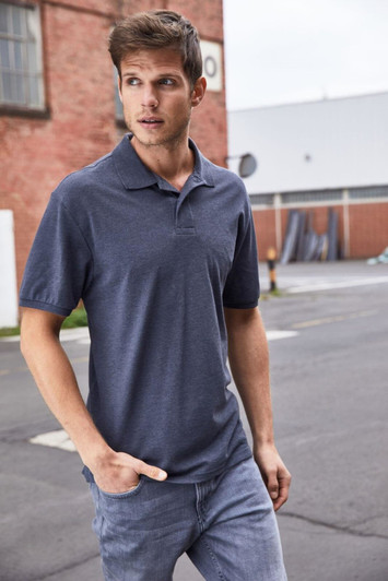A man wearing a dark grey polo shirt and light jeans, standing outdoors with a casual pose.