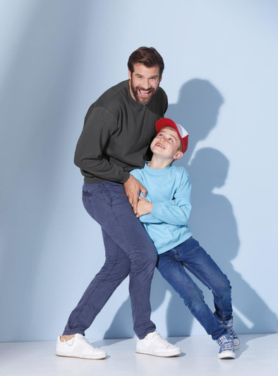 A man in a dark green jumper and a boy in a light blue jumper playfully pose against a blue background.