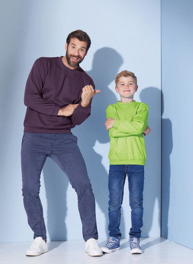 A man in a dark purple jumper and a boy in a bright green jumper pose together against a light blue background.
