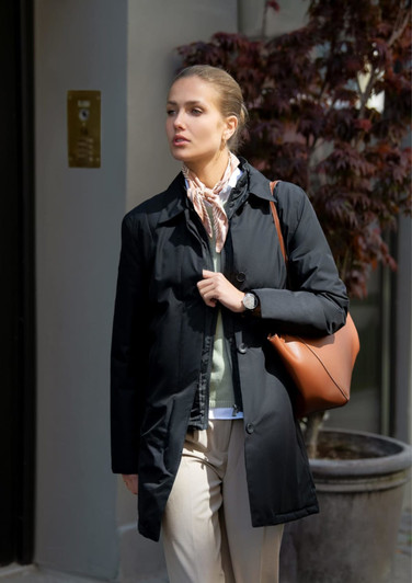 A black women's jacket is worn by a model outdoors, paired with a light-coloured scarf and a brown handbag.