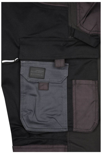 Close-up of black workwear stretch-pants featuring grey pockets and a branded label.