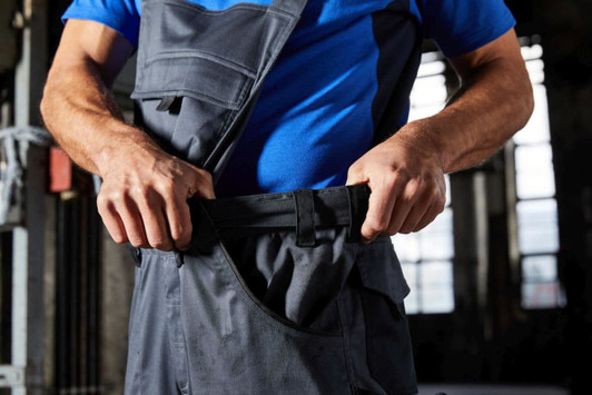Workwear pants with bib in dark grey, featuring pockets and adjustable straps, being worn by a person.
