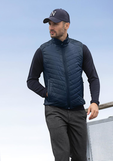 A navy blue men's vest with a quilted design, featuring a zip and side pockets, worn with a black long-sleeve top and cap.