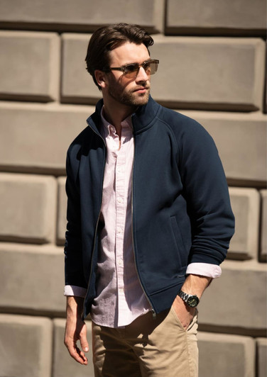 A navy jacket worn over a light pink shirt, modelled by a man with sunglasses against a textured wall.