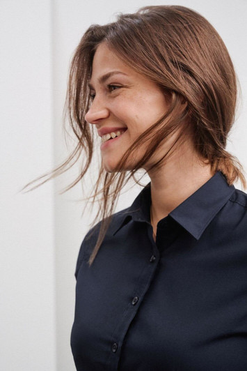 A navy button-up shirt with a sleek design, featuring a collar and buttons, worn by a smiling woman.