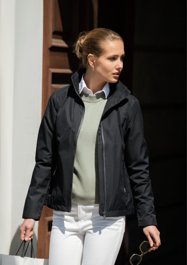 A black women's jacket with a hood, worn over a light green sweater, paired with white pants.