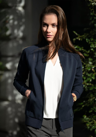 A navy jacket with a zip front and pockets, worn by a model outdoors. The jacket has a simple design and a logo.