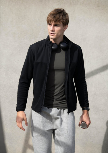A model in grey track pants paired with a black zip-up jacket and headphones, holding a drink bottle.