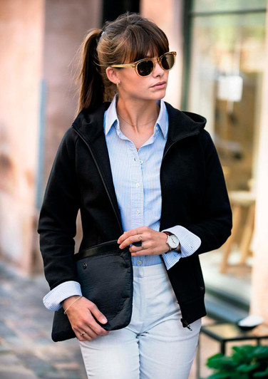 A black women's jacket is worn with a collared shirt. The model accessorises with sunglasses and holds a black clutch.