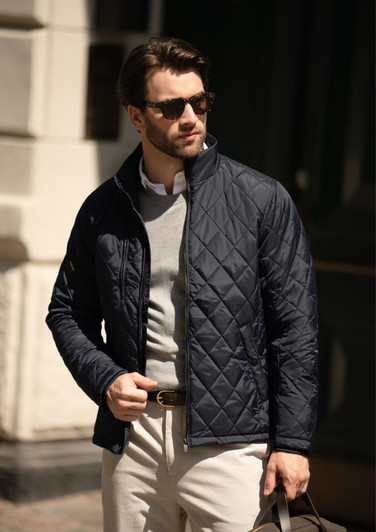 A navy quilted men's jacket features a zip front and a fitted design, worn with a light sweater and beige trousers.