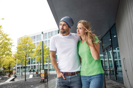 A man in a white shirt and a woman in a green t-shirt stand together outdoors near modern buildings.