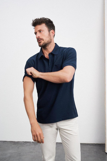A navy polo shirt with a short sleeve, featuring a pocket and a brand logo. Model adjusts the sleeve.