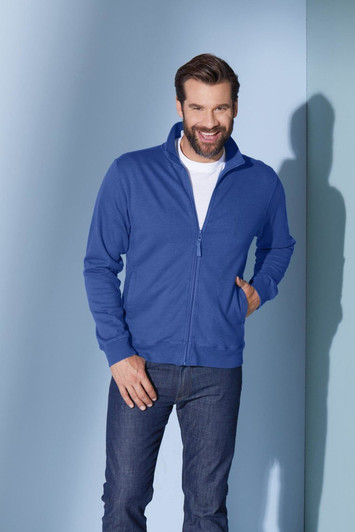 A blue track jacket with a zip, worn by a smiling man against a light background. Features a logo on the jacket.