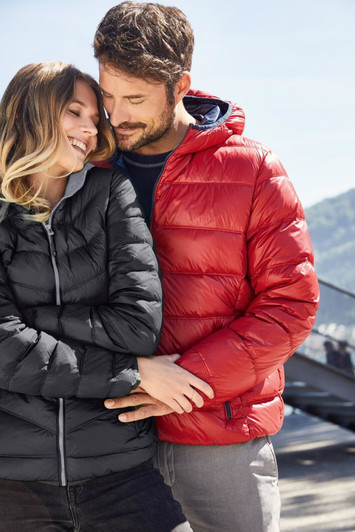 A black puffer jacket and a red puffer jacket modelled by a couple in a scenic outdoor setting. Each jacket features a hood.