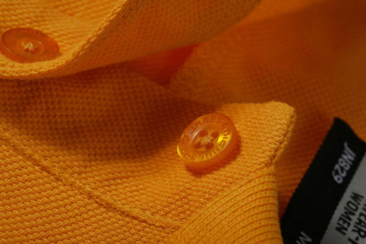 A close-up of an orange work polo shirt featuring a textured fabric and contrasting buttons.