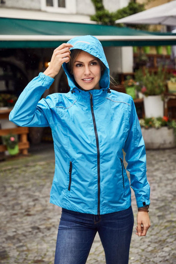 A blue ladies rain jacket with a hood, featuring zippered pockets and worn by a woman outdoors.