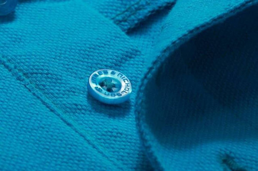 A close-up of a turquoise men's work polo shirt featuring a branded button and textured fabric.