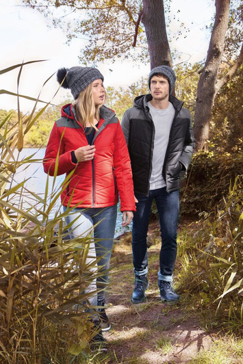 A red puffer jacket worn by a woman and a black puffer jacket worn by a man, both outdoors near trees.