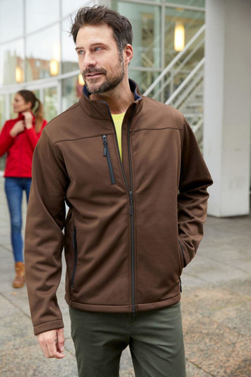 A men's softshell jacket in brown, featuring a zippered chest pocket and a high collar, worn by a man outdoors.