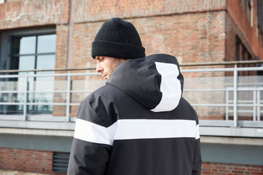 A men's winter sport jacket in black with white stripes, featuring a hood, worn by a person from the back.