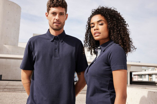 Two models wearing navy plain polo shirts outdoors, standing side by side against a modern architectural backdrop.