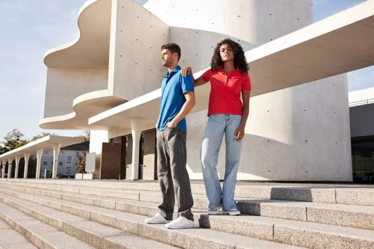 A blue and a red men's mercerised polo shirt displayed on two models against a contemporary architectural background.