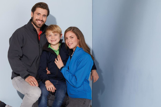 A family wearing softshell jackets in grey, navy, and blue against a light blue background. Each jacket has a logo.