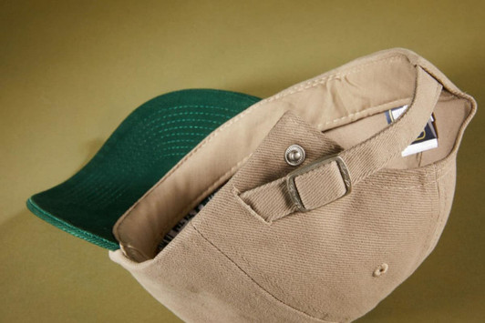 A beige 6 panel cap with a green peak, featuring an adjustable strap and a logo inside.